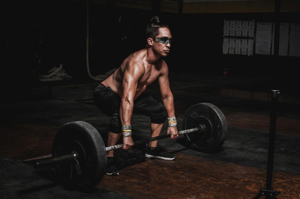 Strong athlete lifting heavy barbell in a dimly lit gym, showcasing strength and determination.